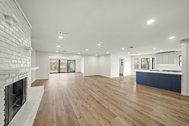 unfurnished living room featuring a brick fireplace, a wealth of natural light, and light wood-type flooring