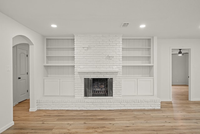 unfurnished living room with a brick fireplace, built in features, ceiling fan, and light hardwood / wood-style flooring