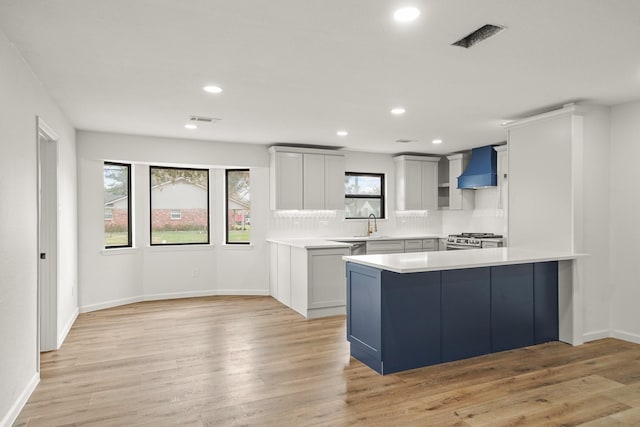 kitchen with tasteful backsplash, a center island, light hardwood / wood-style floors, stainless steel range with gas stovetop, and wall chimney exhaust hood