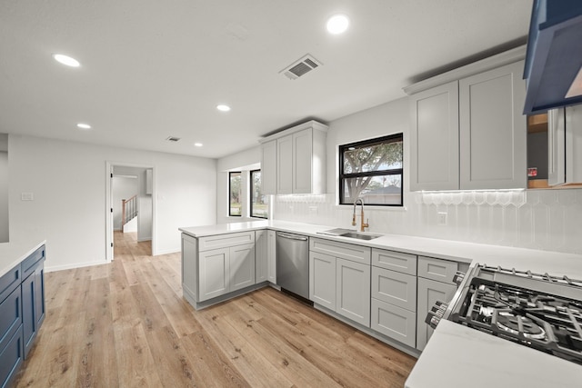 kitchen with appliances with stainless steel finishes, sink, backsplash, kitchen peninsula, and light hardwood / wood-style flooring