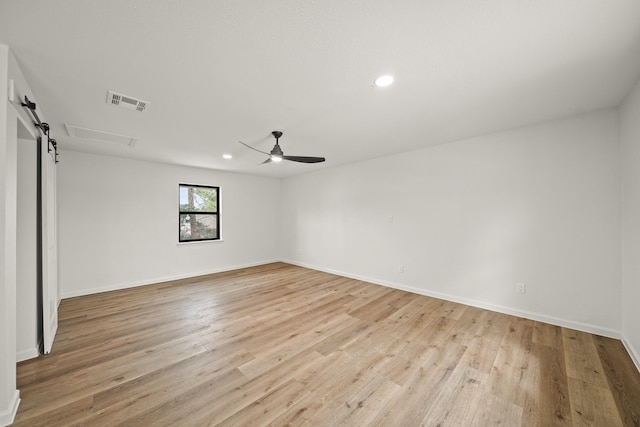 spare room with light hardwood / wood-style floors, a barn door, and ceiling fan