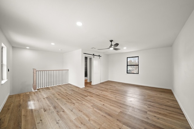 spare room with ceiling fan, a barn door, and light hardwood / wood-style floors