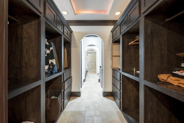 spacious closet featuring stone tile flooring, arched walkways, and a raised ceiling