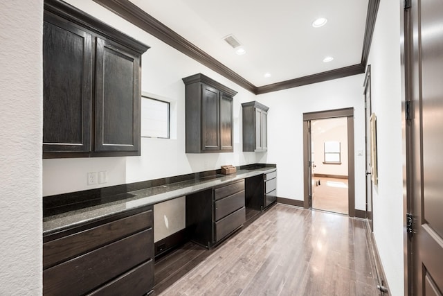 kitchen featuring light wood-style floors, crown molding, baseboards, and built in desk