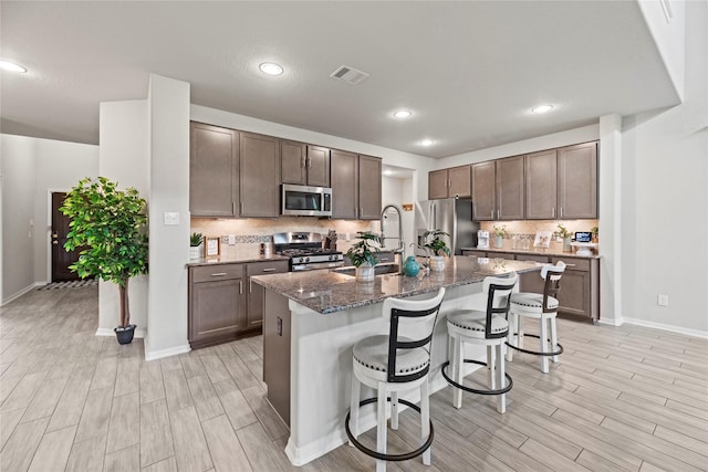 kitchen featuring appliances with stainless steel finishes, dark stone countertops, a kitchen breakfast bar, tasteful backsplash, and a center island with sink