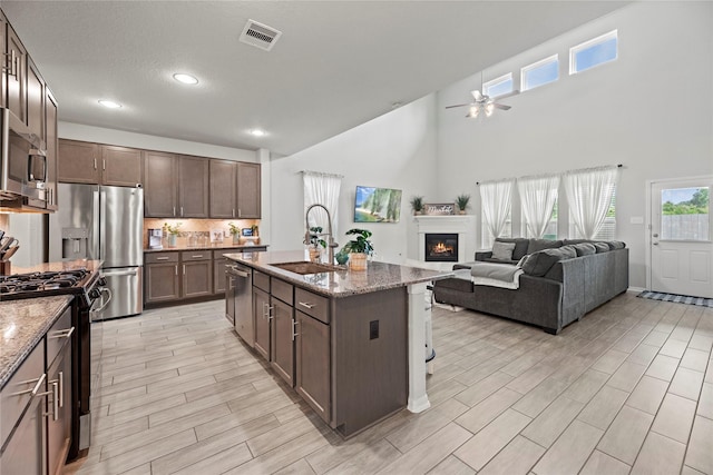 kitchen with an island with sink, appliances with stainless steel finishes, sink, and stone countertops