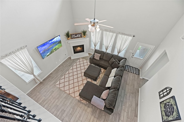 living room with ceiling fan, a towering ceiling, and light hardwood / wood-style floors