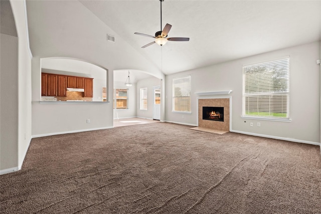 unfurnished living room with a tiled fireplace, high vaulted ceiling, ceiling fan, and carpet flooring