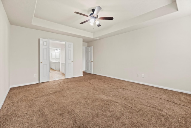 interior space with a tray ceiling, light colored carpet, and ceiling fan