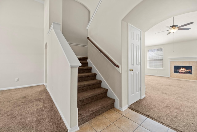 stairs featuring vaulted ceiling, ceiling fan, carpet floors, and a tile fireplace