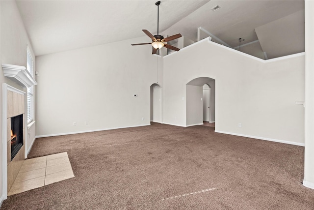 unfurnished living room with a tiled fireplace, high vaulted ceiling, dark carpet, and ceiling fan