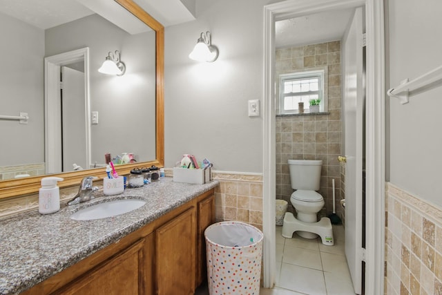 bathroom featuring tile walls, toilet, wainscoting, vanity, and tile patterned floors