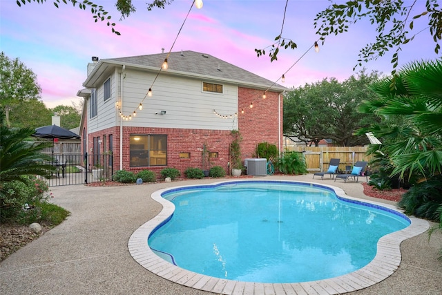 pool at dusk with a patio and central air condition unit