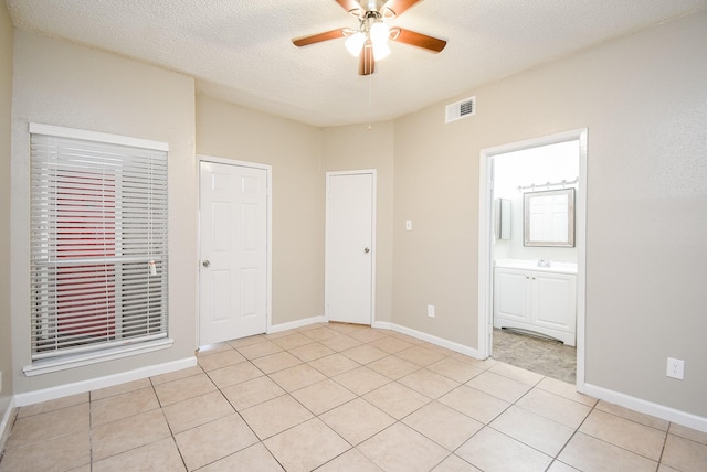 unfurnished bedroom with connected bathroom, light tile patterned floors, a textured ceiling, and ceiling fan