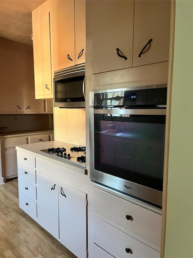 kitchen with a textured ceiling, stainless steel appliances, white cabinets, light wood-style floors, and light countertops