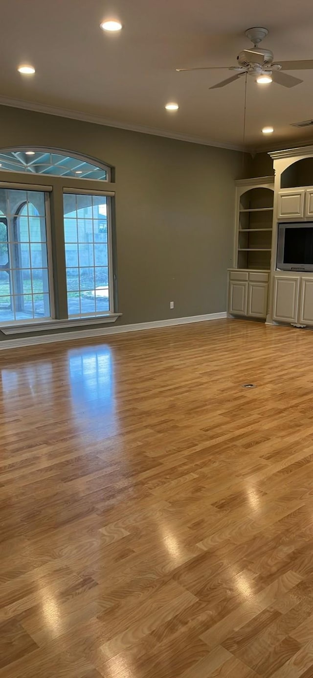 unfurnished living room featuring a ceiling fan, baseboards, crown molding, and light wood finished floors