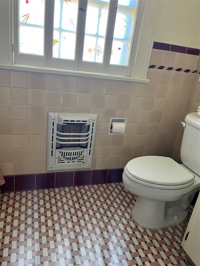 bathroom with heating unit, tile patterned flooring, toilet, and tile walls