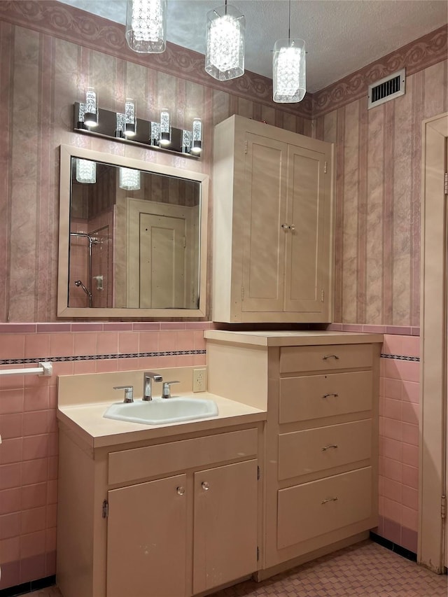 bathroom with wallpapered walls, visible vents, a textured ceiling, and vanity