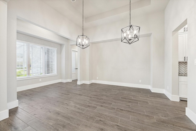 unfurnished dining area featuring dark hardwood / wood-style flooring, a notable chandelier, a tray ceiling, and a high ceiling