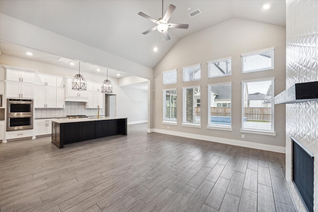 kitchen with pendant lighting, white cabinetry, double oven, a kitchen island with sink, and wood-type flooring