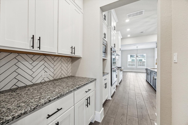 kitchen with dark stone countertops, dark hardwood / wood-style floors, stainless steel microwave, white cabinets, and decorative backsplash