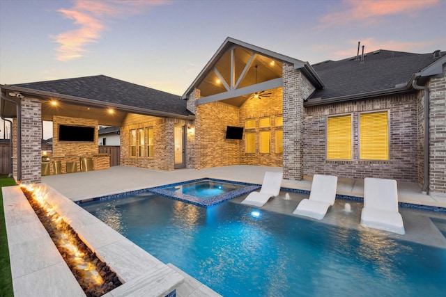 pool at dusk featuring an in ground hot tub, a patio, ceiling fan, and exterior bar