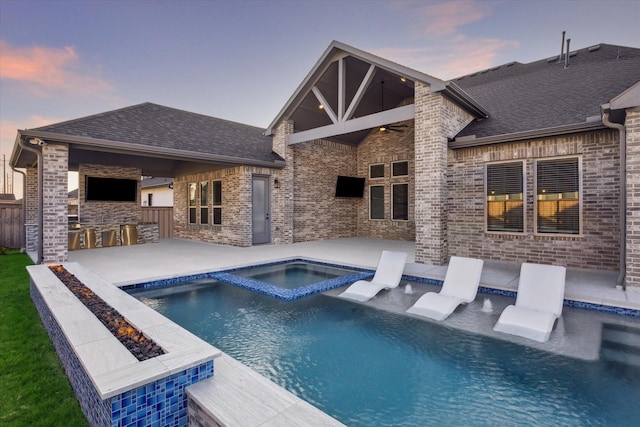 pool at dusk featuring a bar, a patio, and an in ground hot tub