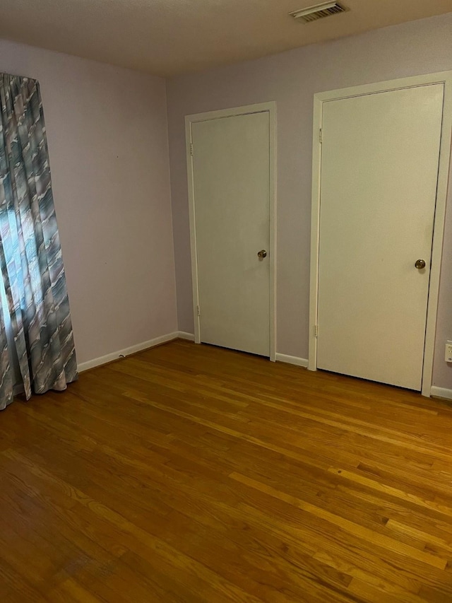 unfurnished bedroom featuring visible vents, baseboards, and wood finished floors