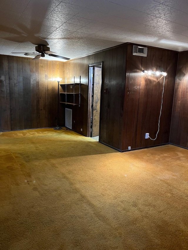 basement featuring light carpet, ceiling fan, and wood walls