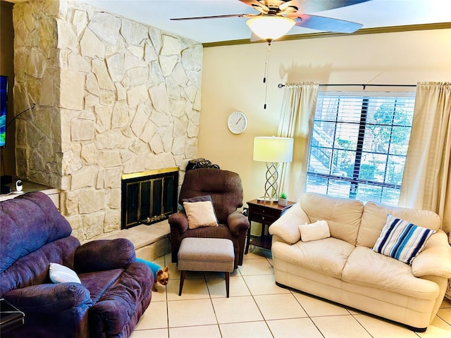 living area with tile patterned floors, a ceiling fan, and a stone fireplace