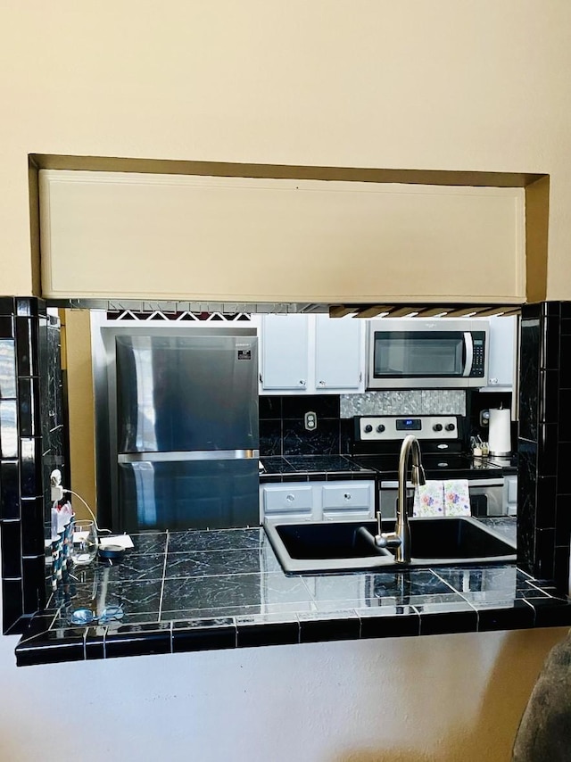 kitchen with stainless steel appliances, a sink, white cabinets, backsplash, and tile counters