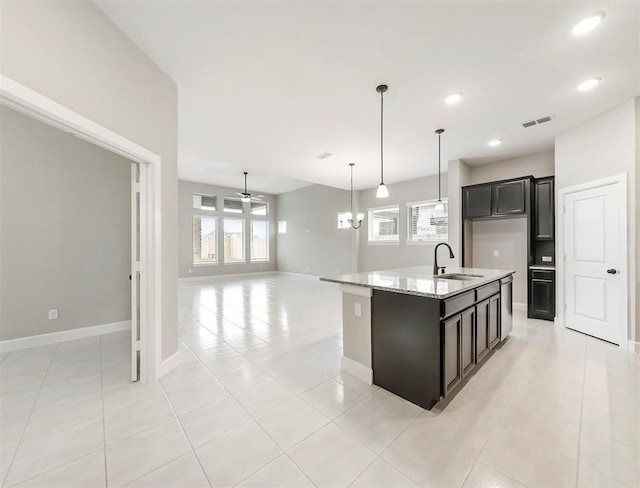 kitchen with pendant lighting, sink, light tile patterned floors, light stone countertops, and a center island with sink