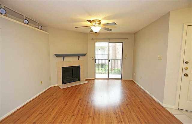 unfurnished living room with a fireplace, track lighting, ceiling fan, and light wood-type flooring