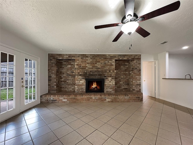 unfurnished living room featuring light tile patterned floors, a textured ceiling, brick wall, a brick fireplace, and french doors