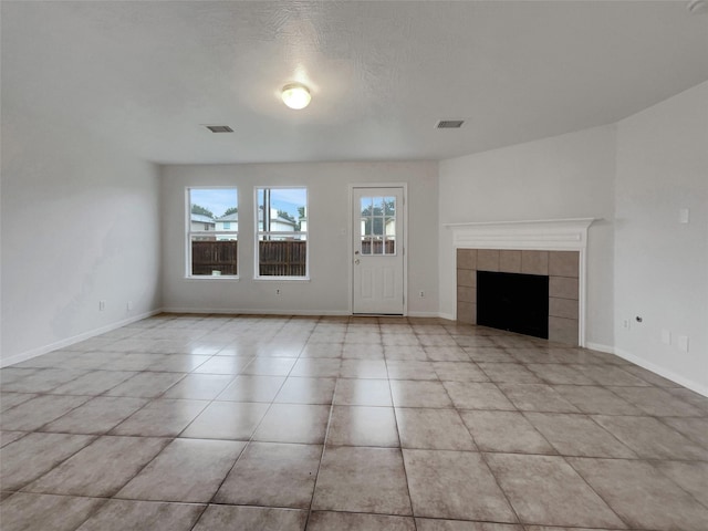 unfurnished living room with a tiled fireplace, light tile patterned floors, and a textured ceiling