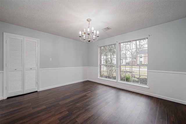 spare room featuring an inviting chandelier, a textured ceiling, and dark hardwood / wood-style flooring