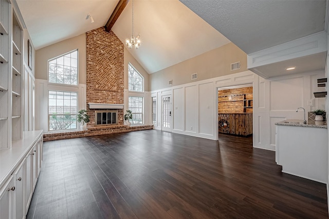 unfurnished living room with beamed ceiling, dark hardwood / wood-style flooring, a brick fireplace, and a notable chandelier