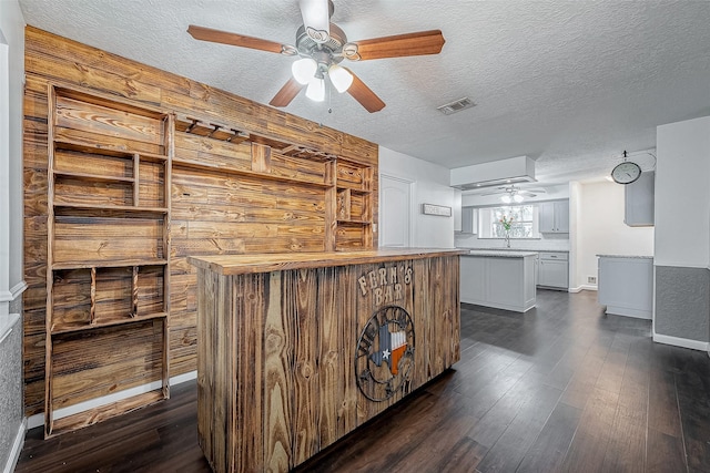 bar with dark hardwood / wood-style flooring, ceiling fan, butcher block counters, and a textured ceiling