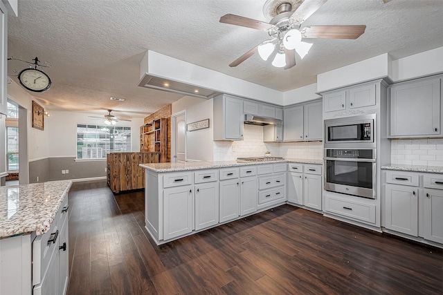 kitchen with stainless steel appliances, light stone countertops, dark hardwood / wood-style floors, and kitchen peninsula