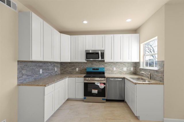 kitchen featuring appliances with stainless steel finishes, sink, white cabinets, decorative backsplash, and light stone counters