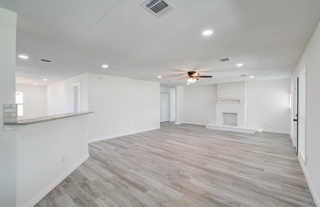 unfurnished living room with a brick fireplace, ceiling fan, and light hardwood / wood-style flooring