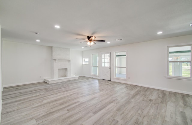 unfurnished living room with ceiling fan, light hardwood / wood-style flooring, a brick fireplace, and a wealth of natural light