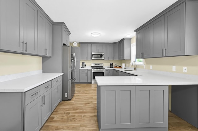 kitchen featuring sink, light hardwood / wood-style flooring, appliances with stainless steel finishes, gray cabinetry, and kitchen peninsula