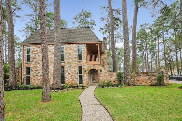 view of front of home with a shingled roof, a front yard, brick siding, and a balcony