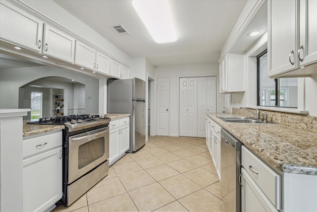 kitchen featuring light tile patterned flooring, appliances with stainless steel finishes, sink, white cabinets, and light stone counters