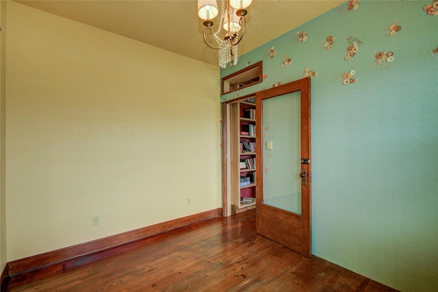 empty room with hardwood / wood-style flooring, a notable chandelier, and a textured ceiling