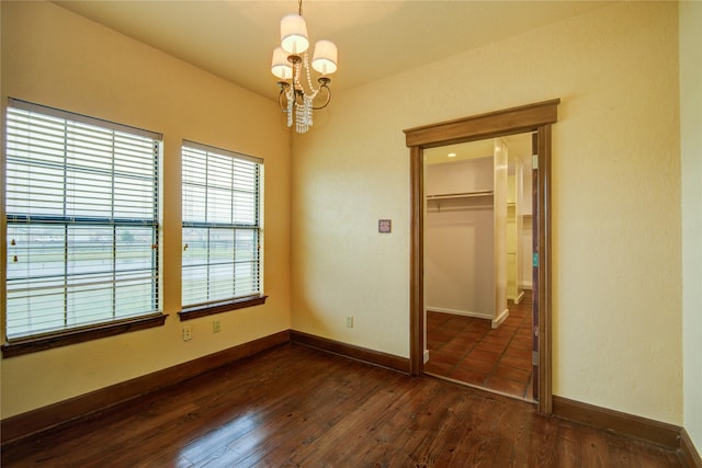 spare room featuring a notable chandelier and dark wood-type flooring