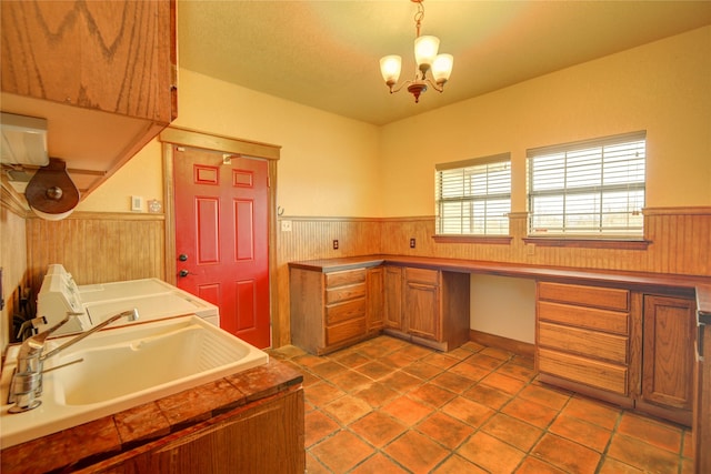 kitchen featuring sink, wood walls, an inviting chandelier, built in desk, and hanging light fixtures