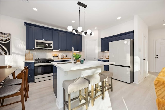 kitchen with blue cabinetry, gas stove, tasteful backsplash, white refrigerator, and an island with sink