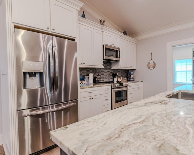 kitchen with appliances with stainless steel finishes, tasteful backsplash, white cabinets, ornamental molding, and light stone counters